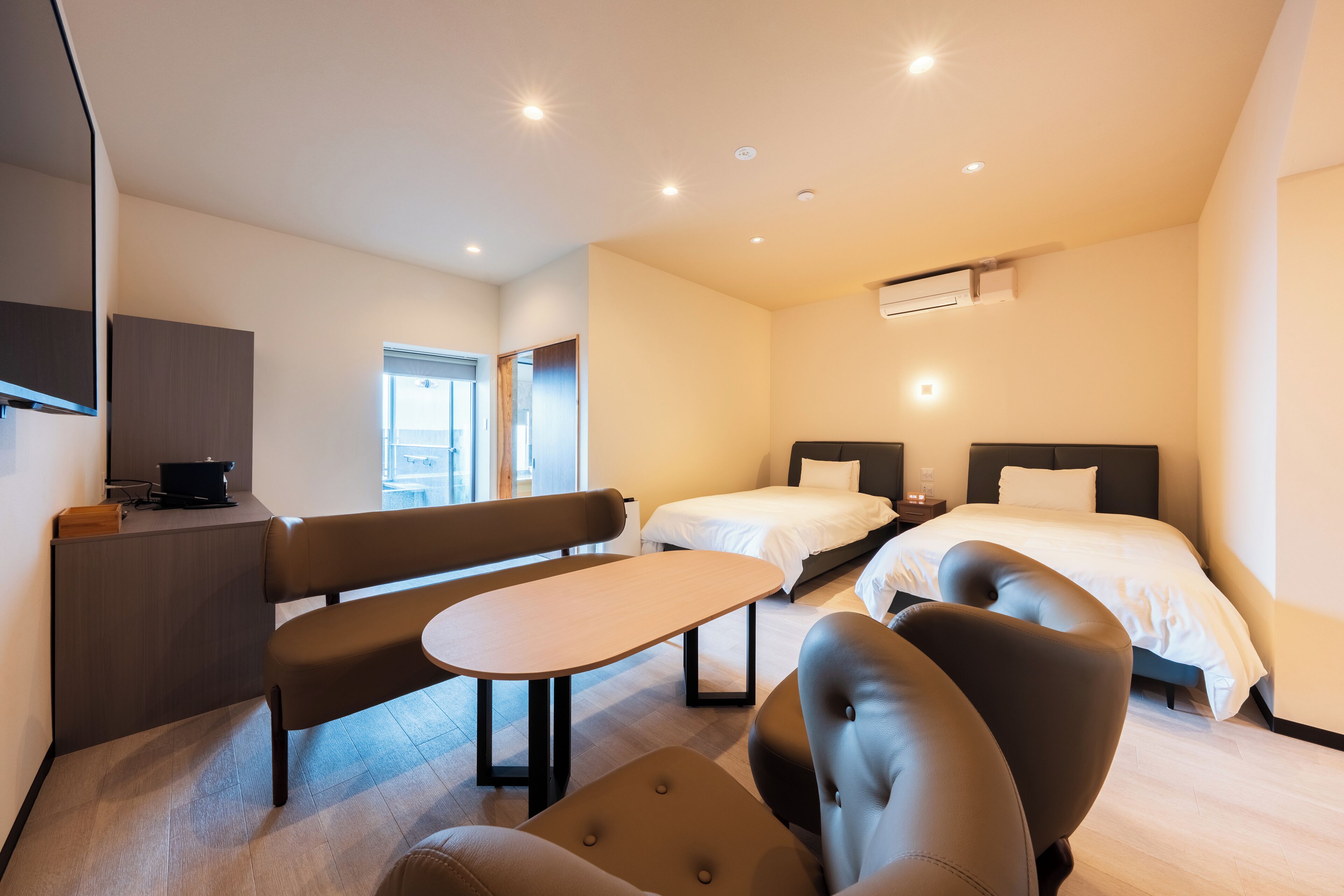 A modern hotel room with a bed, a desk, a bench, and a chair.