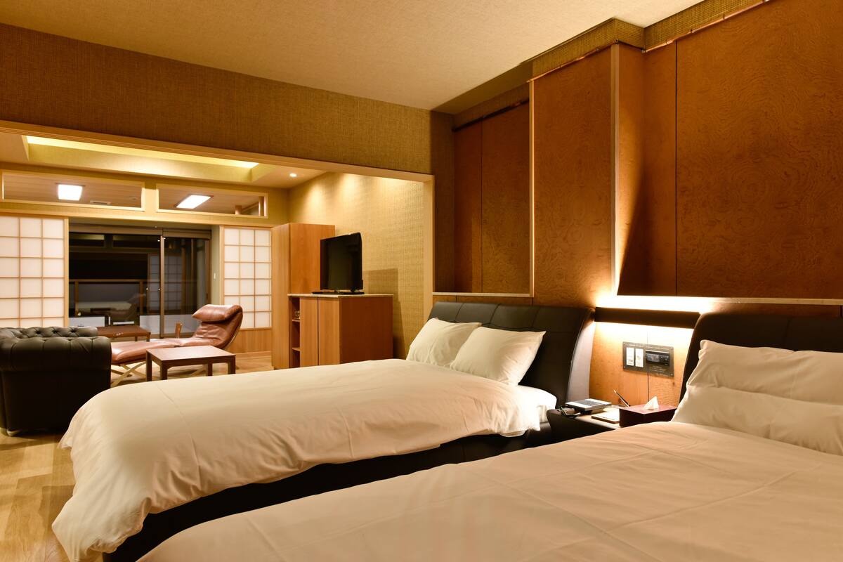 A hotel room with two beds, a desk, a chair, and a television.