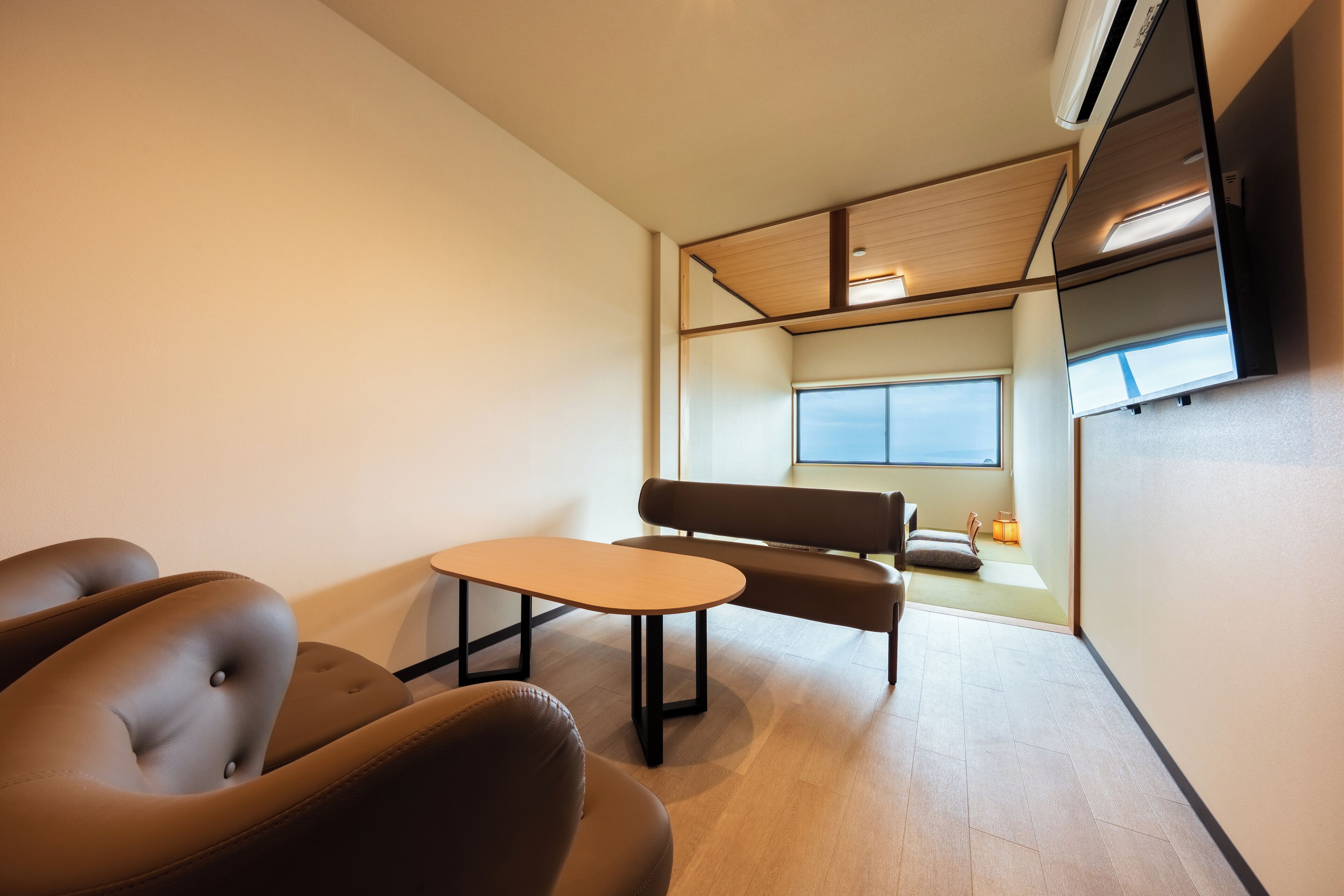 A modern, minimalist living room with a sofa, two armchairs, a small table, and a large window providing natural light.
