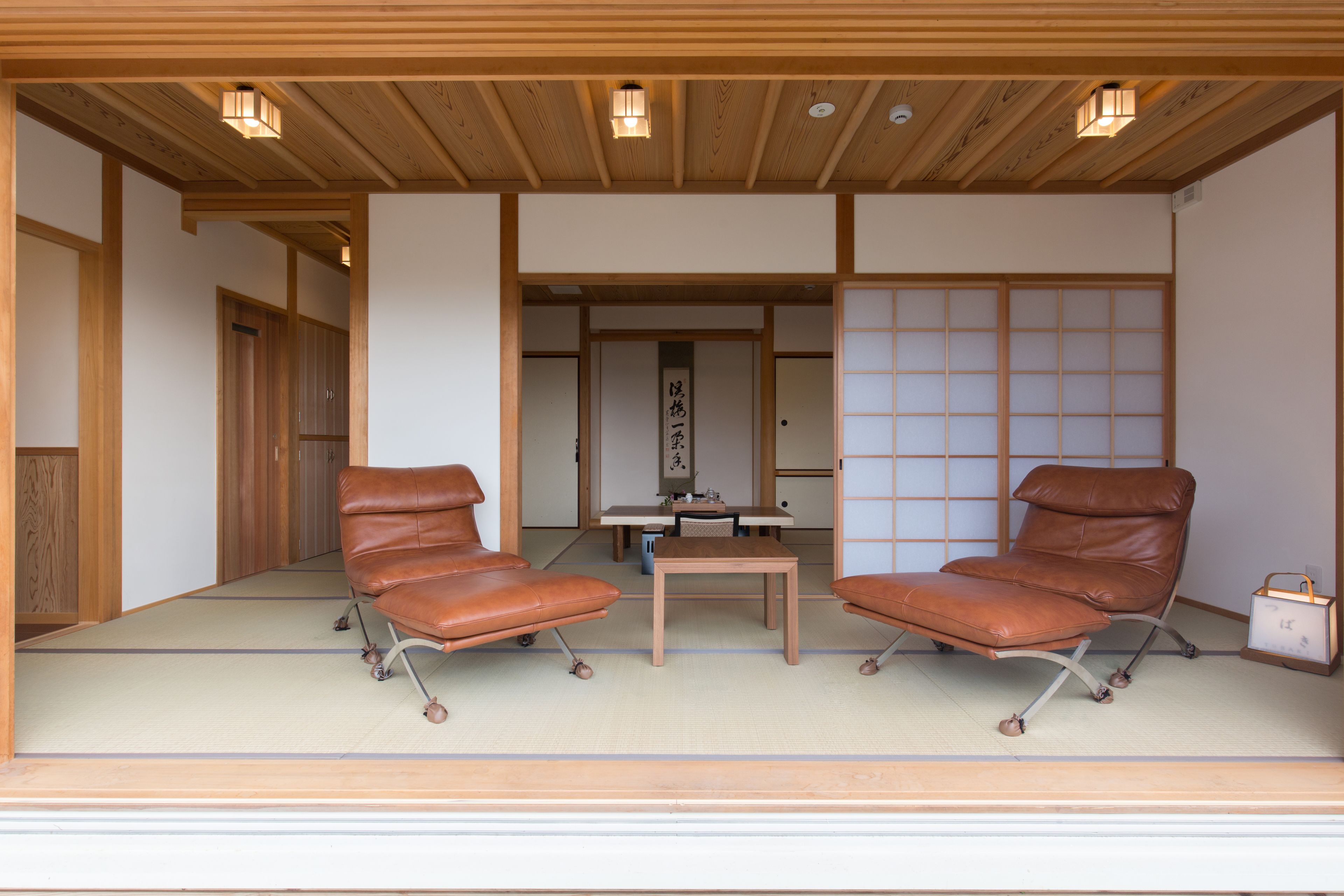 A traditional Japanese room with tatami flooring, two leather chairs, a small table, and a shoji screen.