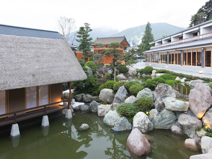 A traditional Japanese garden with a stone bridge, koi pond, and a building with sliding doors.