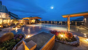 Zona de piscina en la azotea con terraza de madera, asientos y vistas a la ciudad al anochecer.