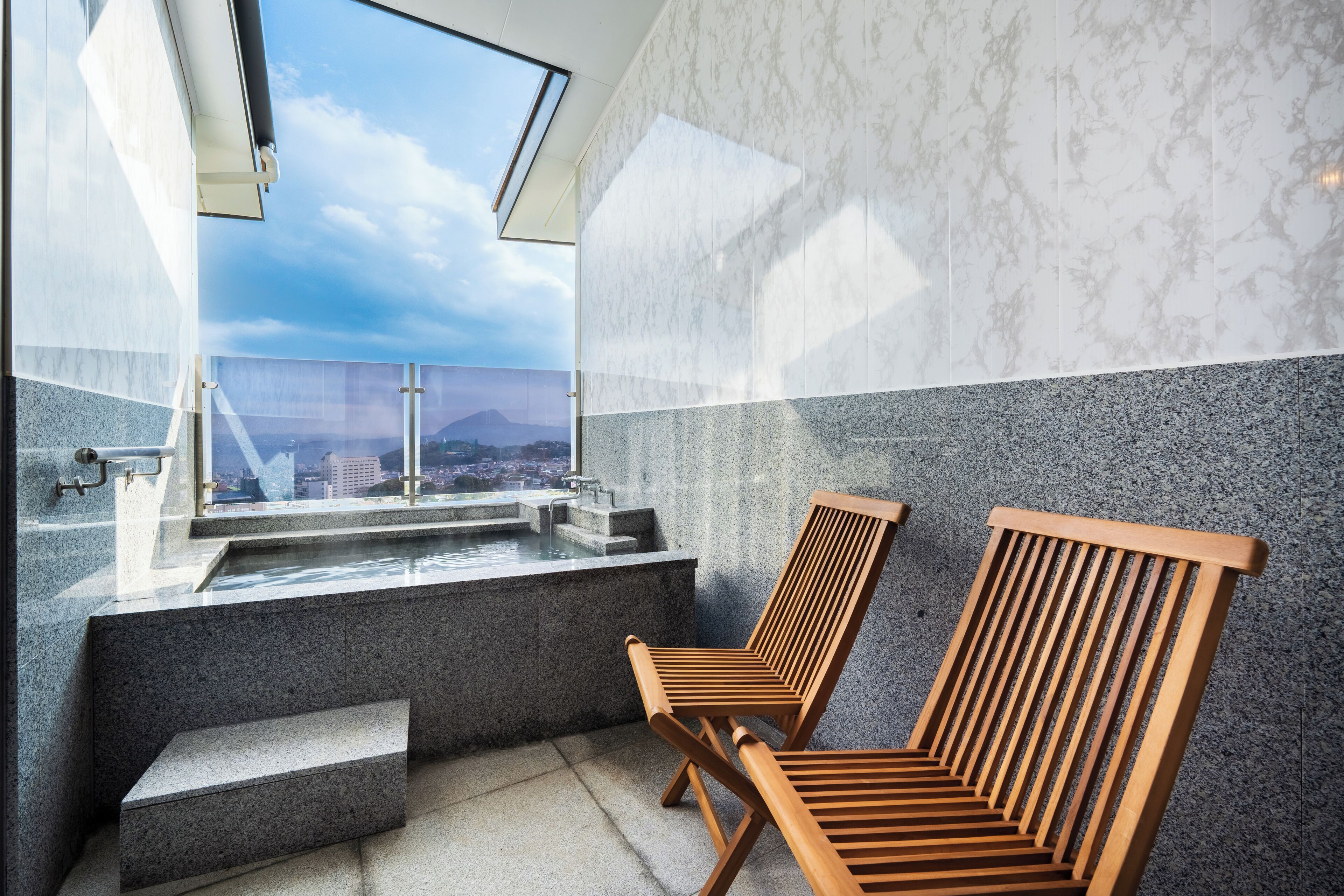 A modern bathroom with a large window, a sink, and two wooden chairs.