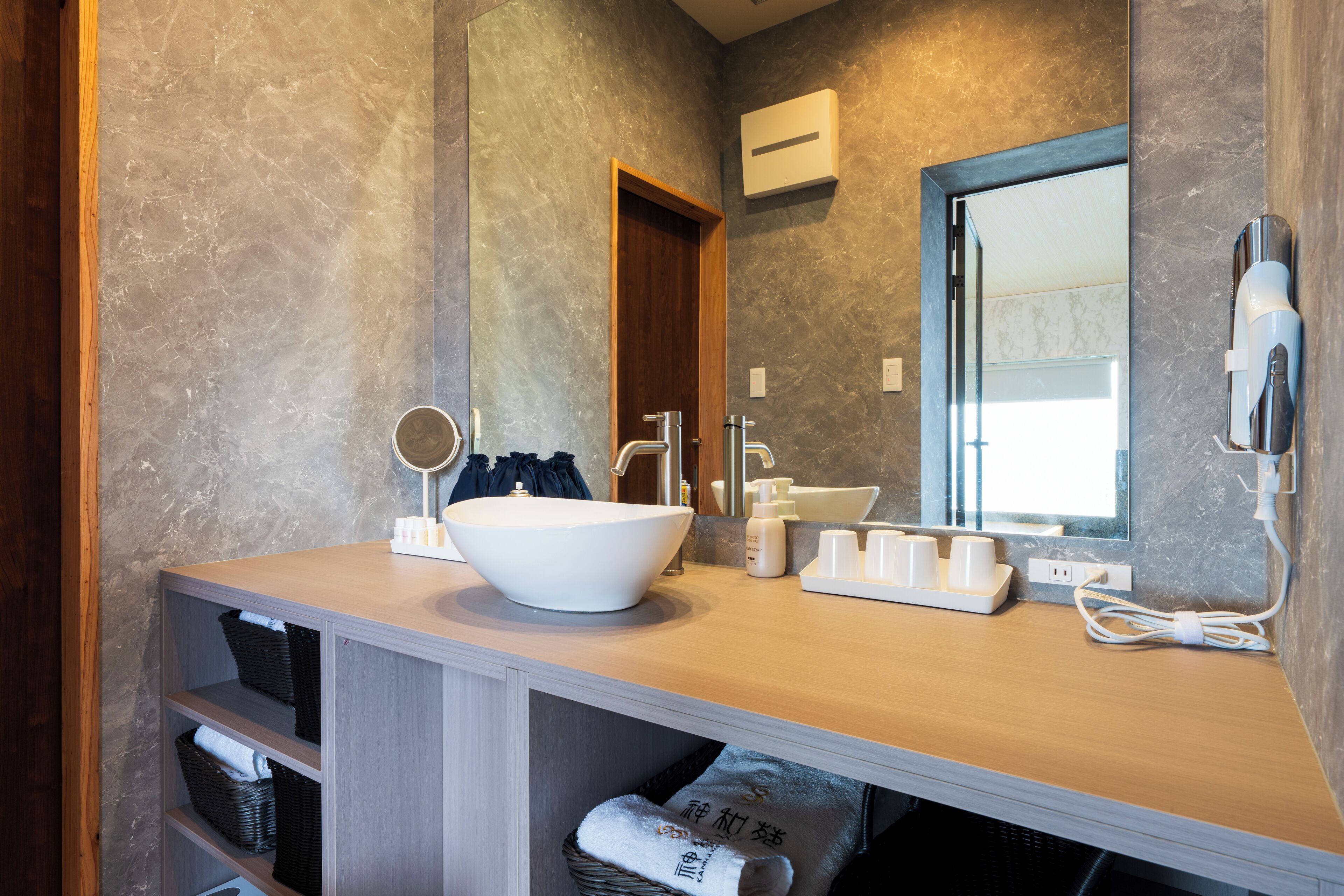 A modern bathroom with a large sink, mirror, and a hairdryer mounted on the wall.