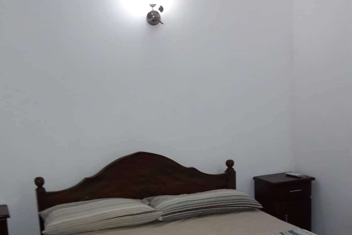 A bedroom with a wooden bed, a bedside table, and a wall-mounted light.