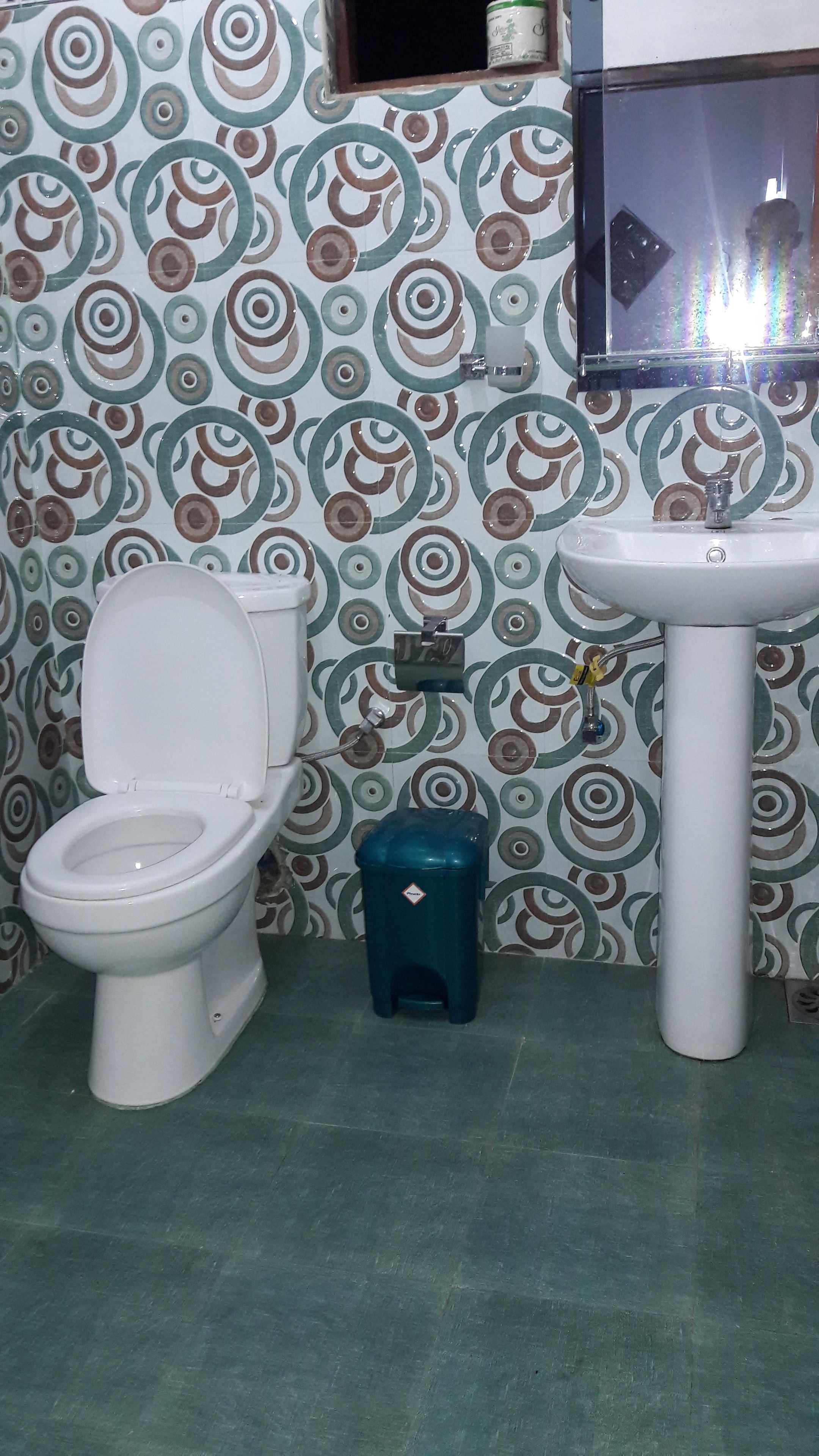 Un baño con inodoro, lavamanos y un cubo de basura azul.