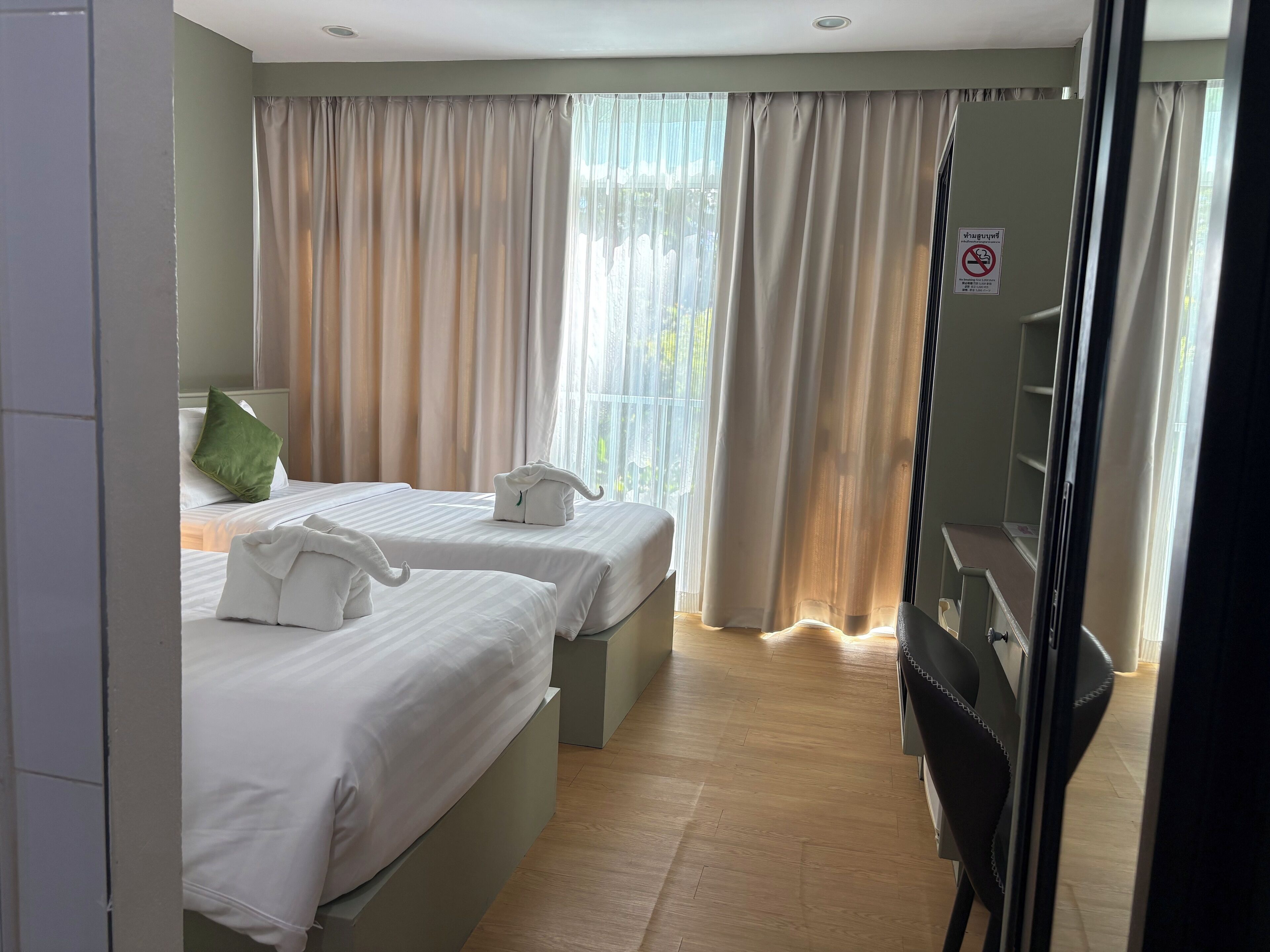 A hotel room with two beds, a green pillow, a towel, and a sign prohibiting smoking.