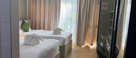 A hotel room with two beds, a green pillow, a towel, and a sign prohibiting smoking.