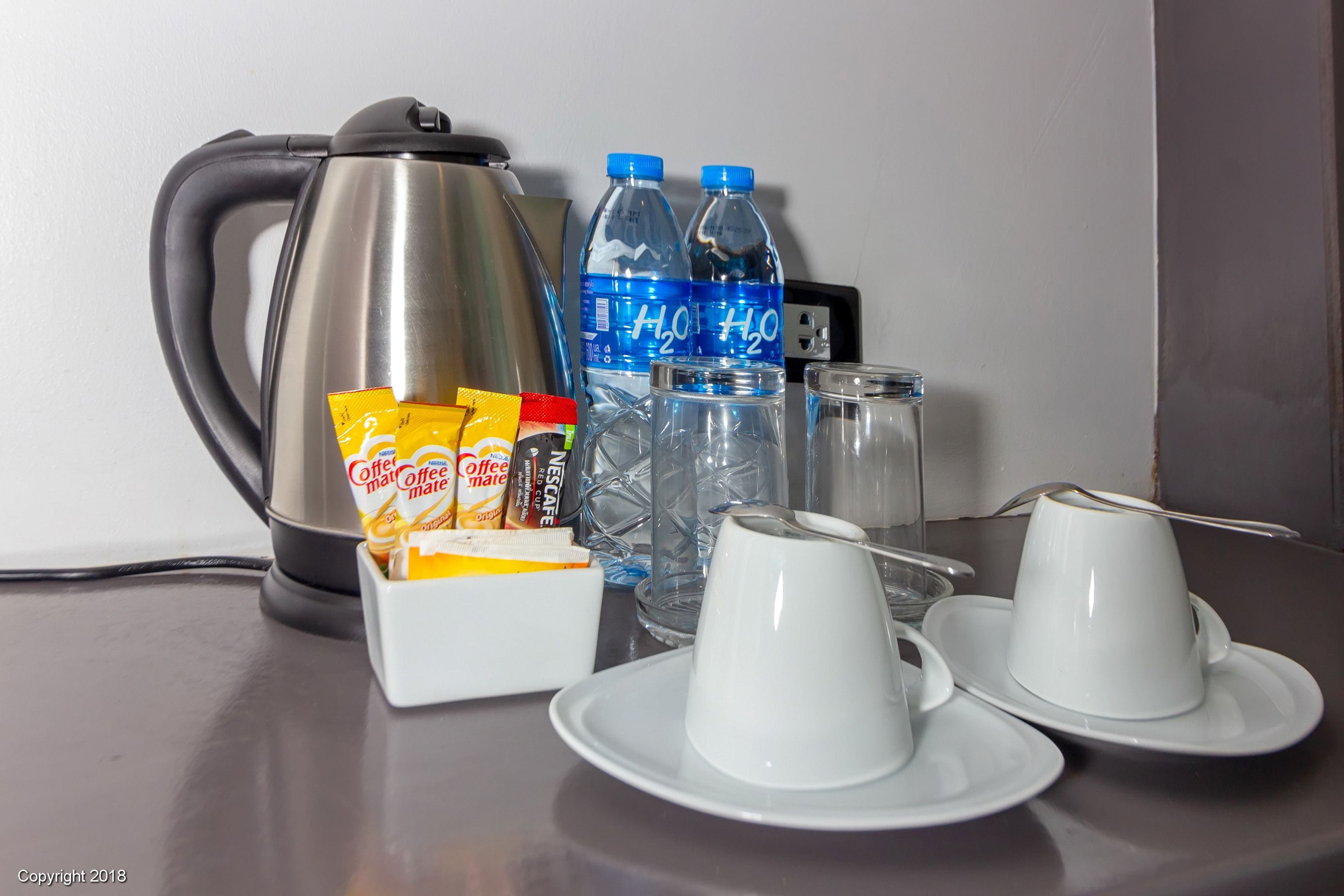 A coffee maker, two water bottles, a coffee mug, a glass, and a box of coffee creamer on a table.