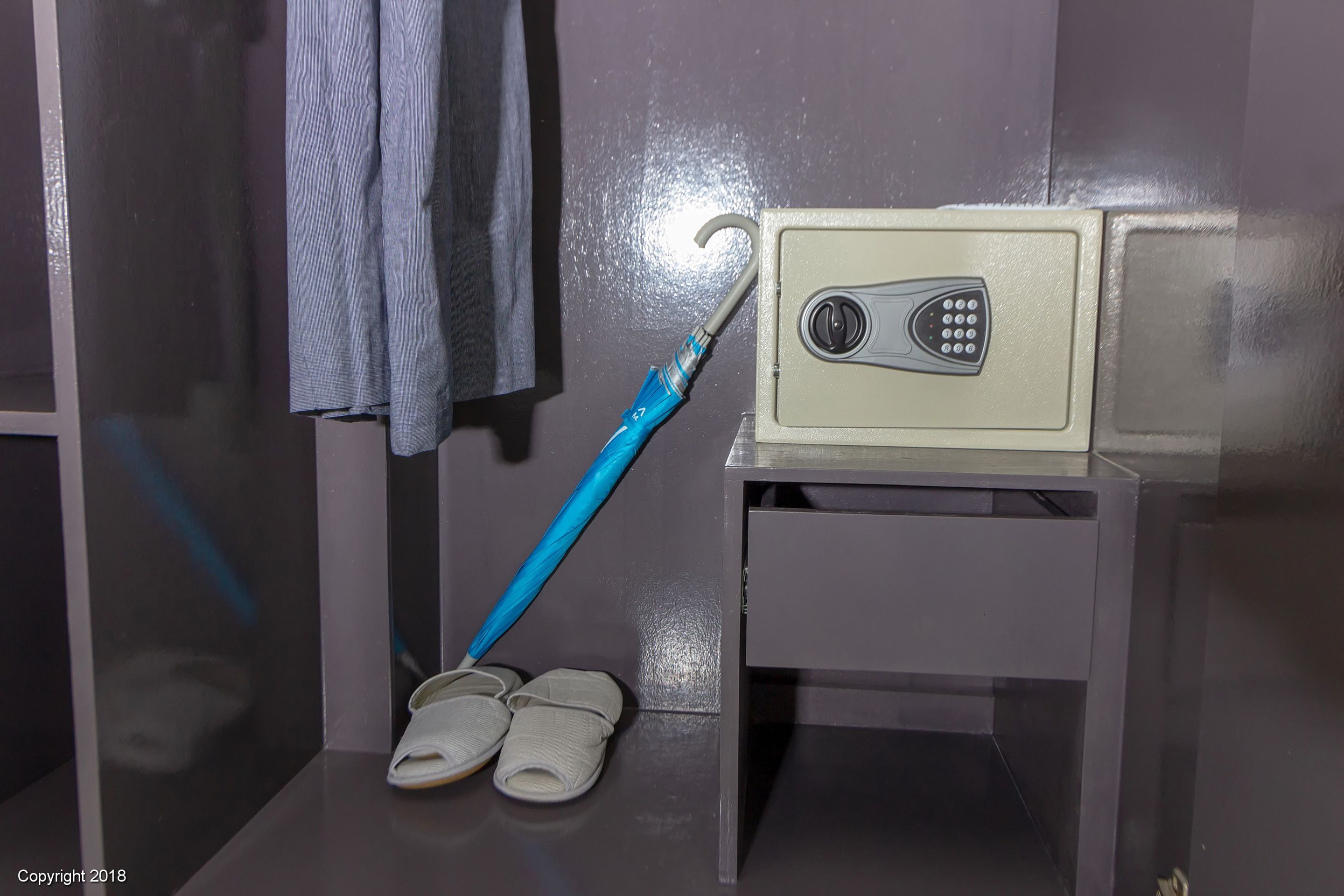 Ein Badezimmer mit einem Handtuch an der Wand, einem blauen Regenschirm, einem Paar Hausschuhen und einem kleinen Schrank mit einem Telefon.