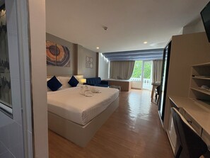 A hotel room with a bed, a desk, a chair, a TV, and a balcony. - Modern Living Hotel (Patong)