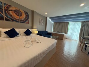 A hotel room with a large bed, a sofa, a small table, a bathtub, and a view of the outdoors. - Modern Living Hotel (Patong)