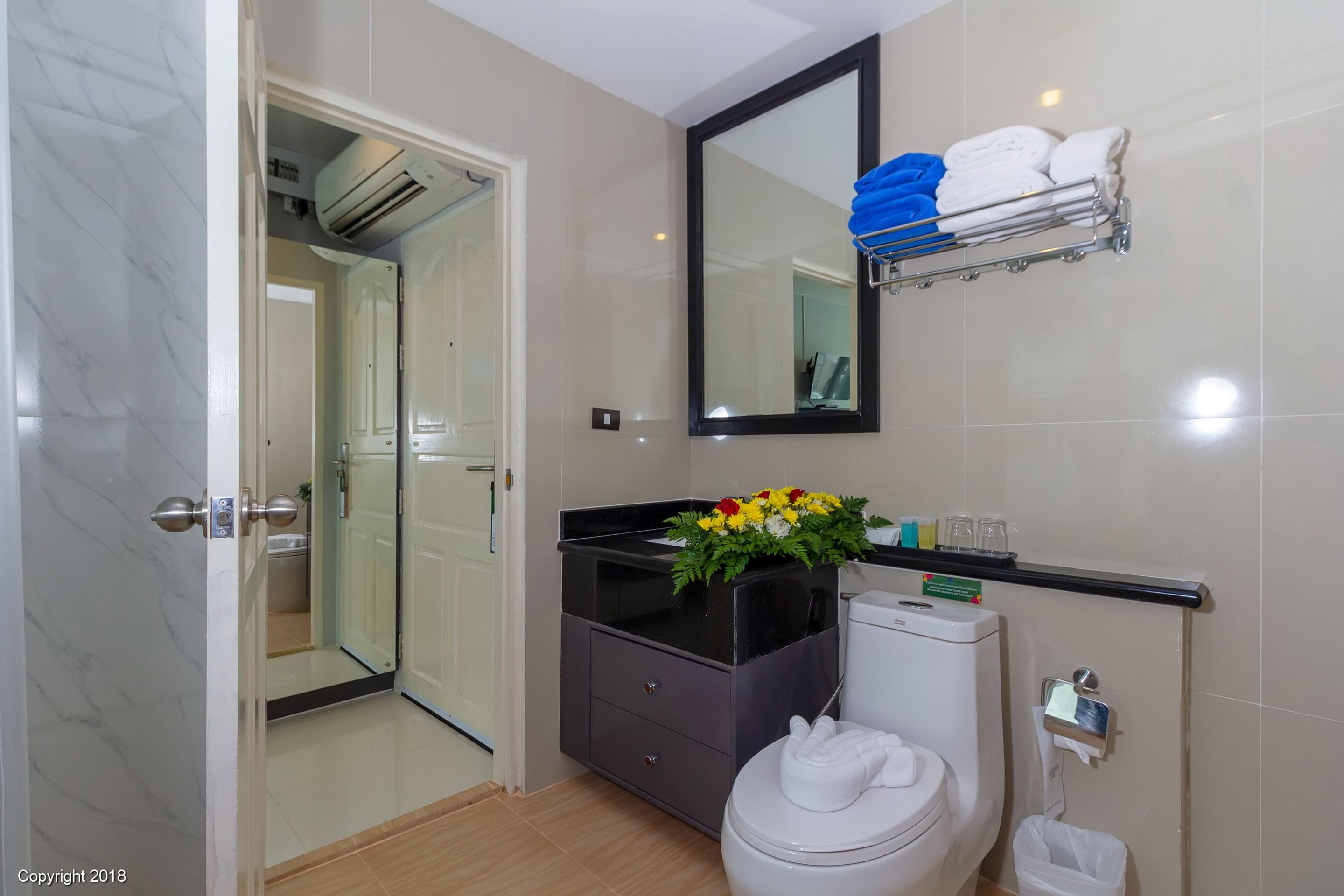 A modern bathroom with a toilet, a vanity with a black countertop, a mirror, and a towel rack with towels.
