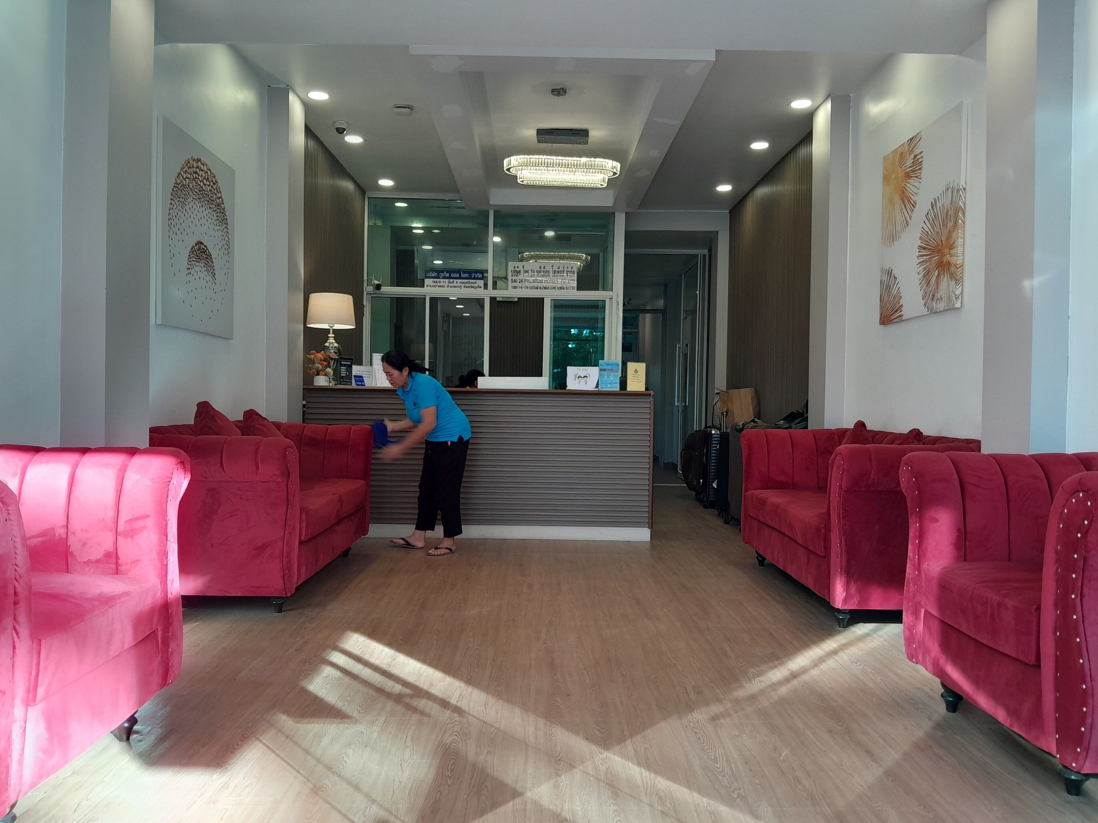 A reception area with a receptionist, red upholstered chairs, a wooden reception desk, and a chandelier.