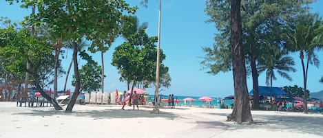 A beach area with trees, umbrellas, and beachgoers.