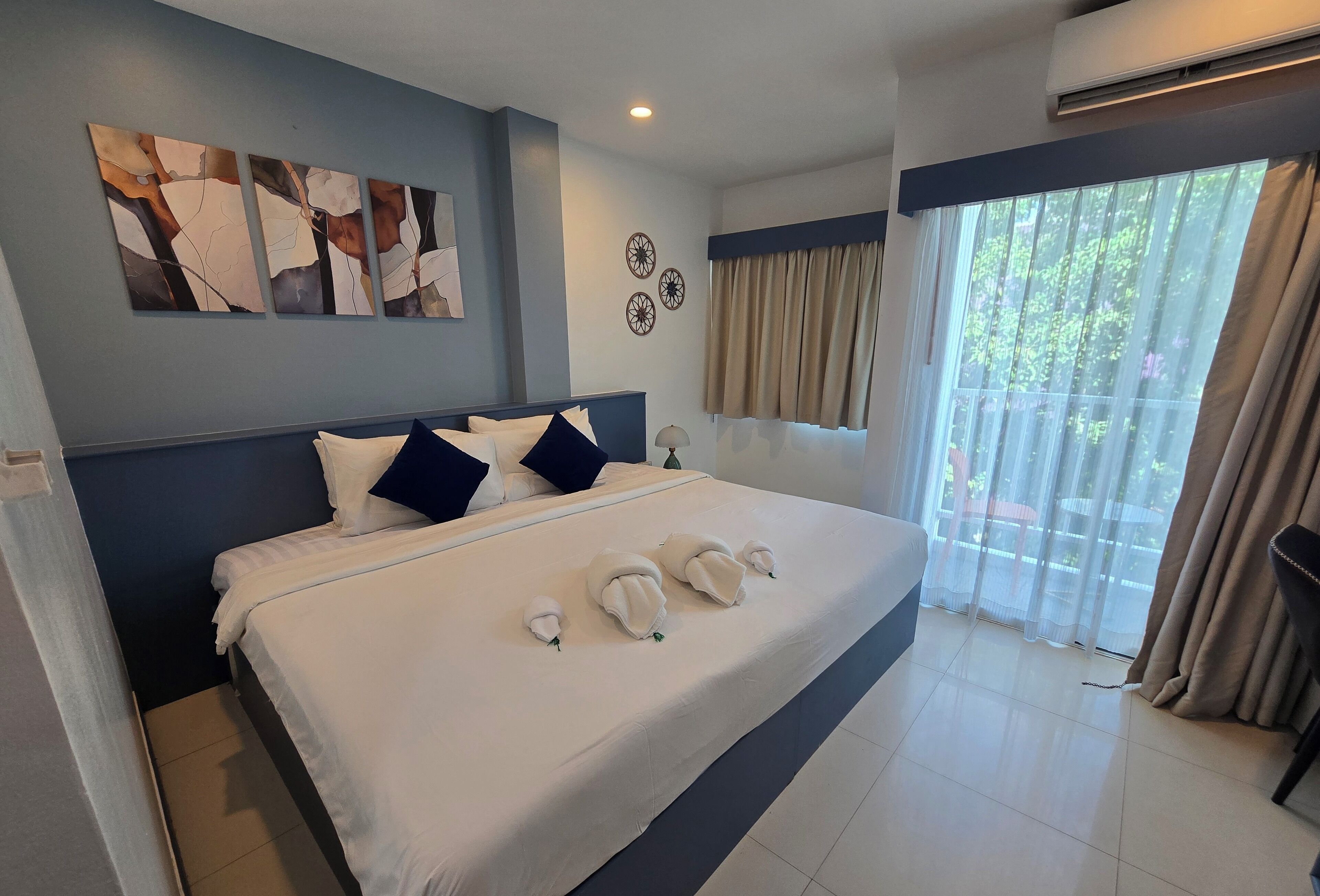 Une chambre d’hôtel avec un grand lit, un ventilateur de plafond, une fenêtre avec des rideaux et un climatiseur fixé au mur.