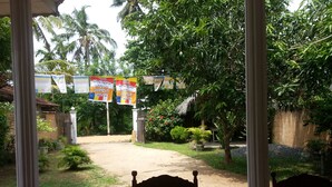 A covered outdoor area with a pathway leading to a gate, surrounded by greenery and palm trees. - Nishan Surf Inn (Matara)