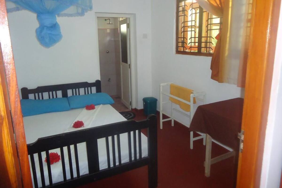 A bedroom with a bed, a desk, and a chair. There is a door leading to another room.