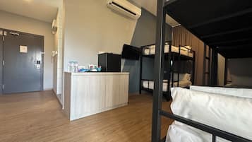 Une chambre avec des lits superposés, un coin cuisine et une porte équipée d’un téléphone et d’un interrupteur pour la lumière.