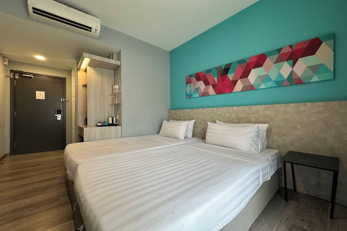 Una camera d'albergo con un letto grande, un comodino, un'opera d'arte appesa al muro e un bagno visibile attraverso una porta aperta.