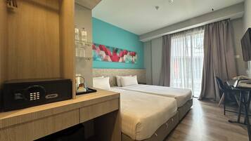 A hotel room with a bed, a desk, a minibar, a TV, and a window with curtains.