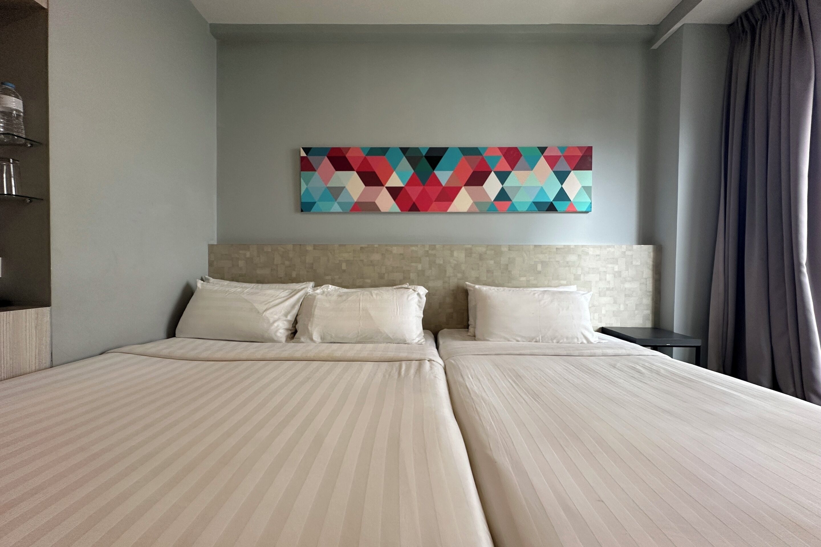 A hotel room with two beds, a headboard, a wall-mounted artwork, and a nightstand.