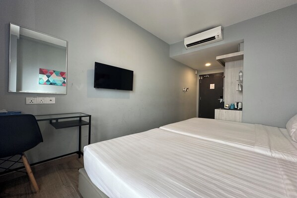 A hotel room with a bed, a desk, a chair, a flat-screen TV, and an air conditioning unit. - OYO Townhouse, Selayang formerly RHR Hotel (Batu Caves)