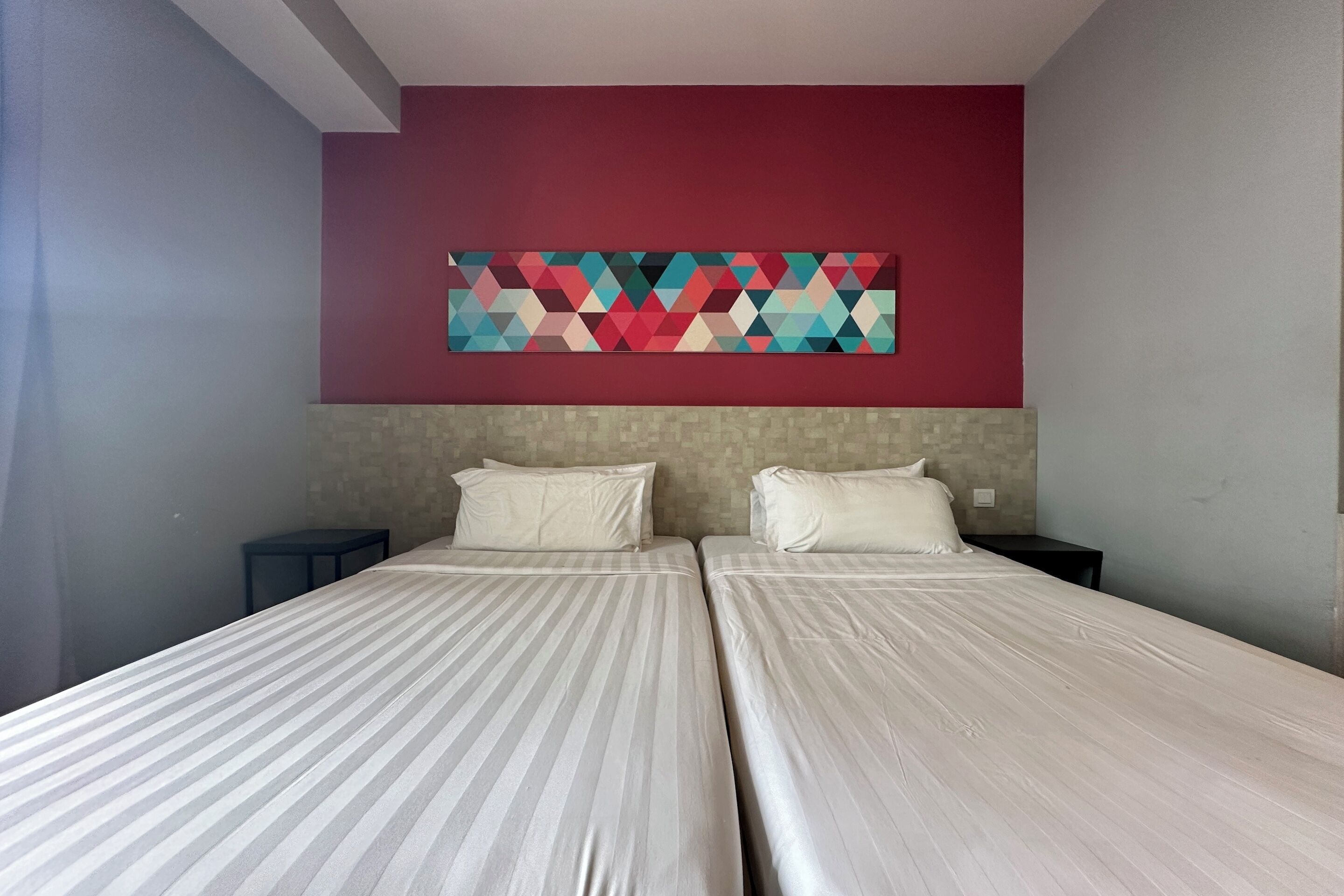 A hotel room with two beds, a red accent wall, and a geometric artwork above the beds.