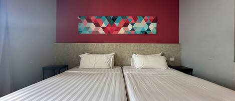 A hotel room with two beds, a red accent wall, and a geometric artwork above the beds.