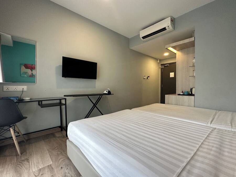 A hotel room with a bed, a desk, a chair, a TV, and an air conditioning unit.