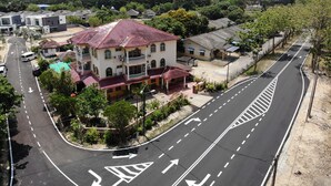 Um edifício com vários andares e telhado de telhas vermelhas, rodeado por uma estrada com setas indicativas e uma calçada.
