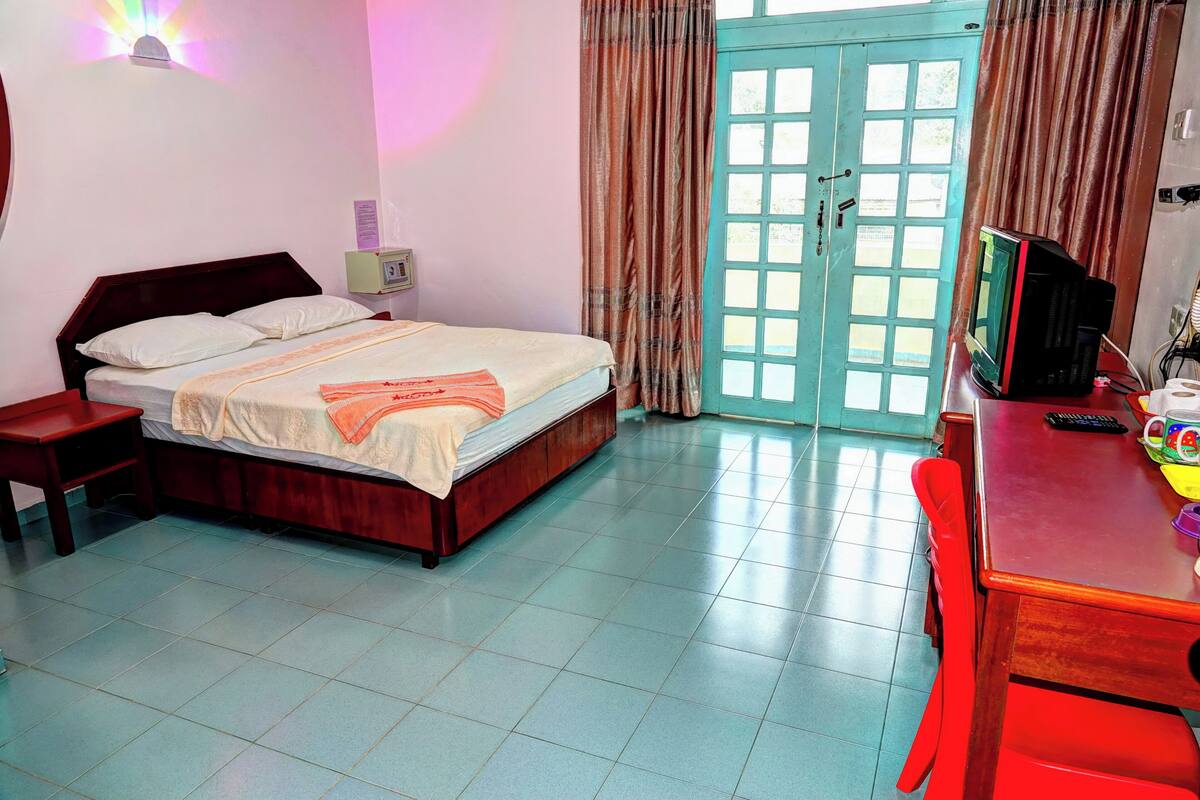 A bedroom with a bed, bedside table, and a TV on a wooden table.