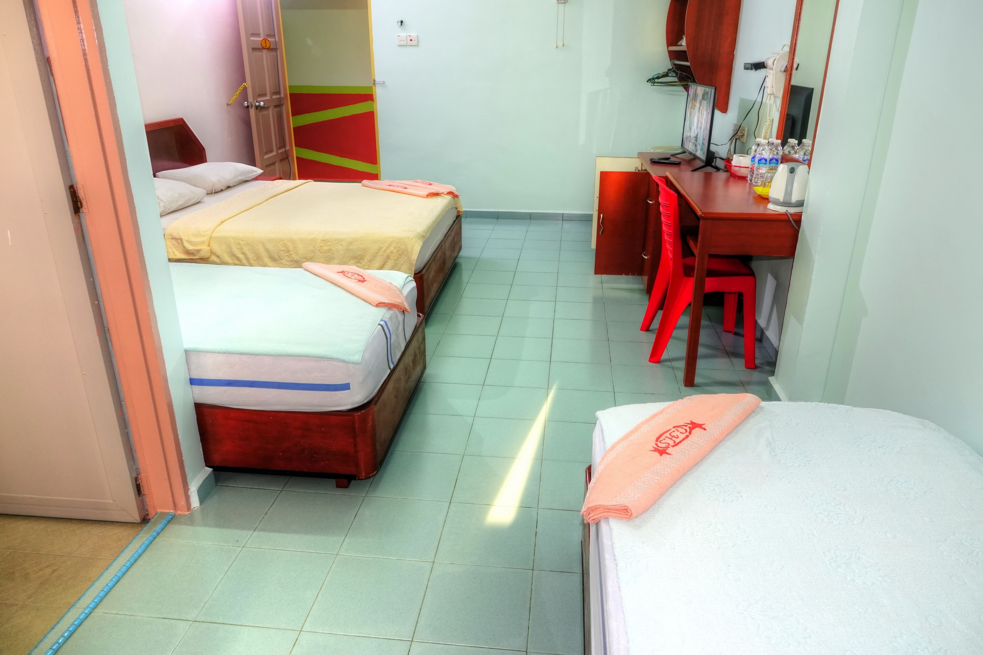 A hotel room with two beds, a desk with a computer, a chair, and a wardrobe.
