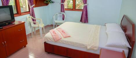 A bedroom with a bed, a TV, a wooden dresser, a chair, and a shelf with clothes.