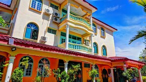 Um edifício de vários andares com varanda, grandes janelas e telhado de telhas vermelhas.