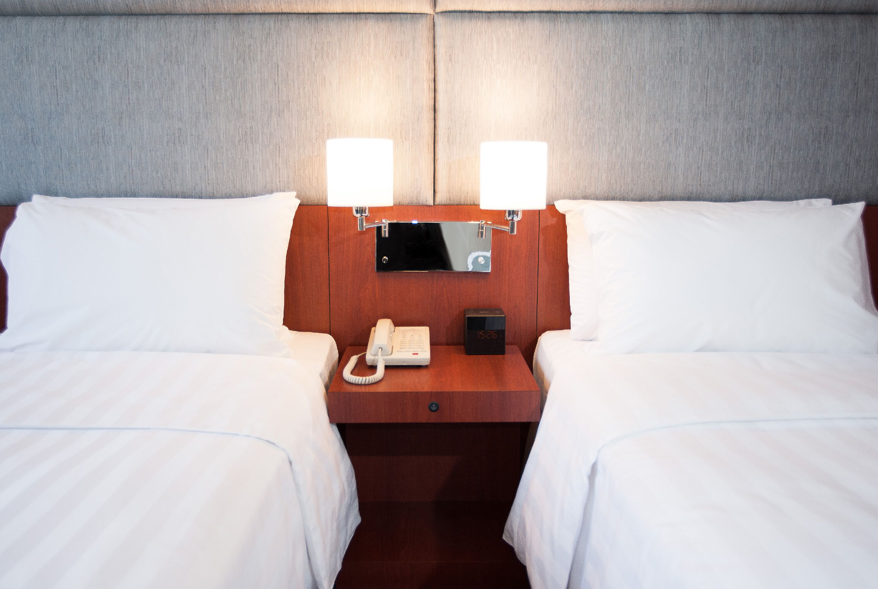 A hotel room with two beds, a wooden nightstand, a bedside telephone, and two wall-mounted lamps.