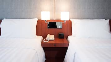 A hotel room with two beds, a wooden nightstand, a bedside telephone, and two wall-mounted lamps.