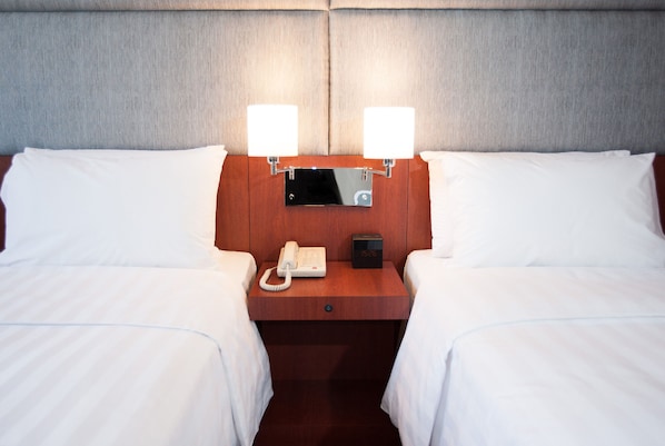 A hotel room with two beds, a wooden nightstand, a bedside telephone, and two wall-mounted lamps.