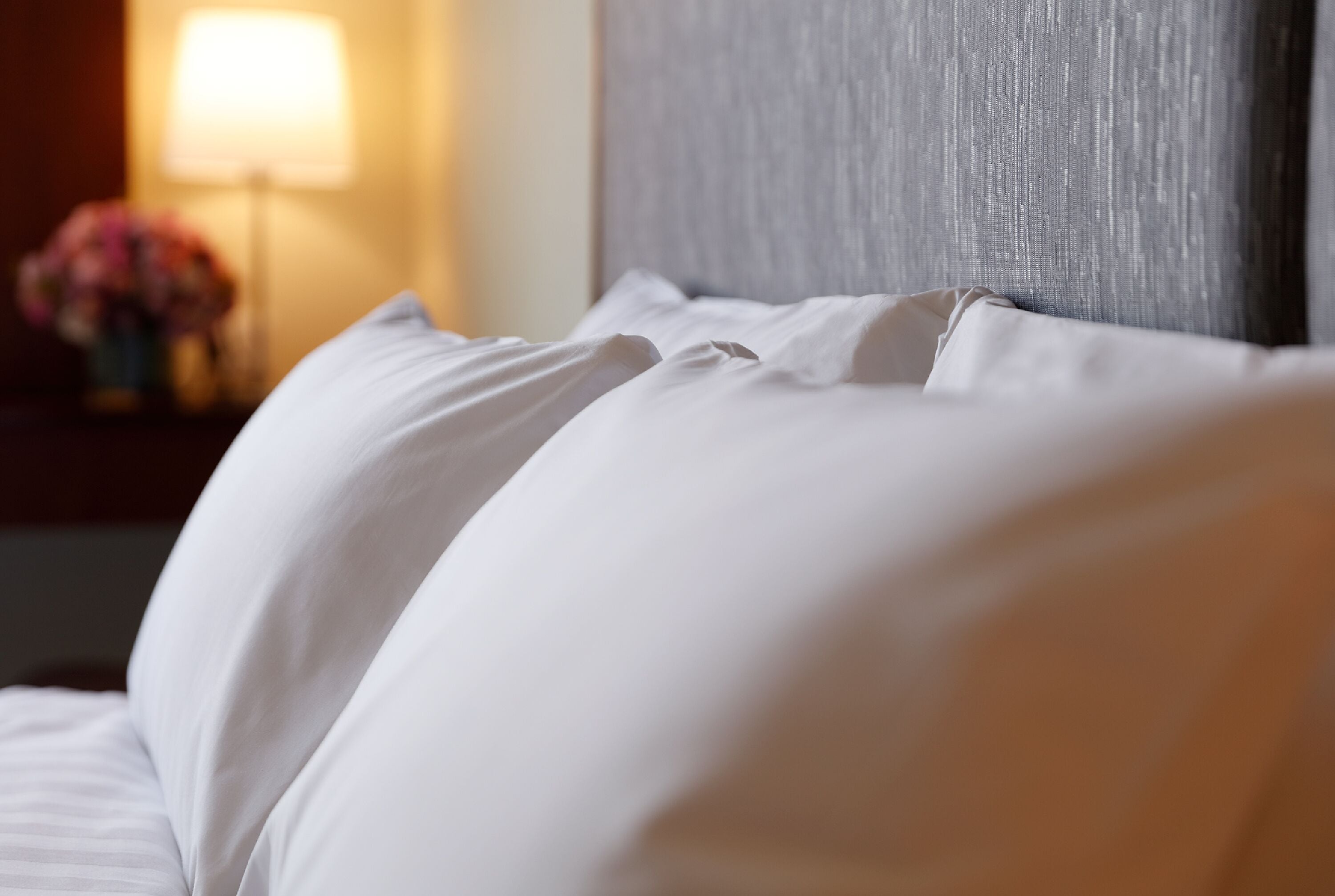 A close-up of a bed with white linens and a grey headboard.
