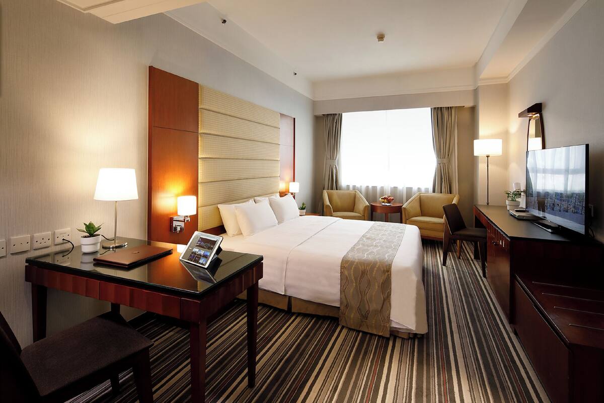 Una habitación de hotel con cama, escritorio, silla, televisor y ventana con cortinas.