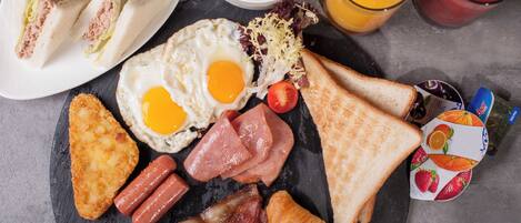 A breakfast plate with eggs, bacon, toast, ham, and a bowl of soup.