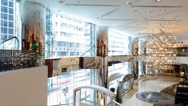 A modern interior with a glass staircase, a central atrium, and a decorative chandelier. - B P International (Kowloon)