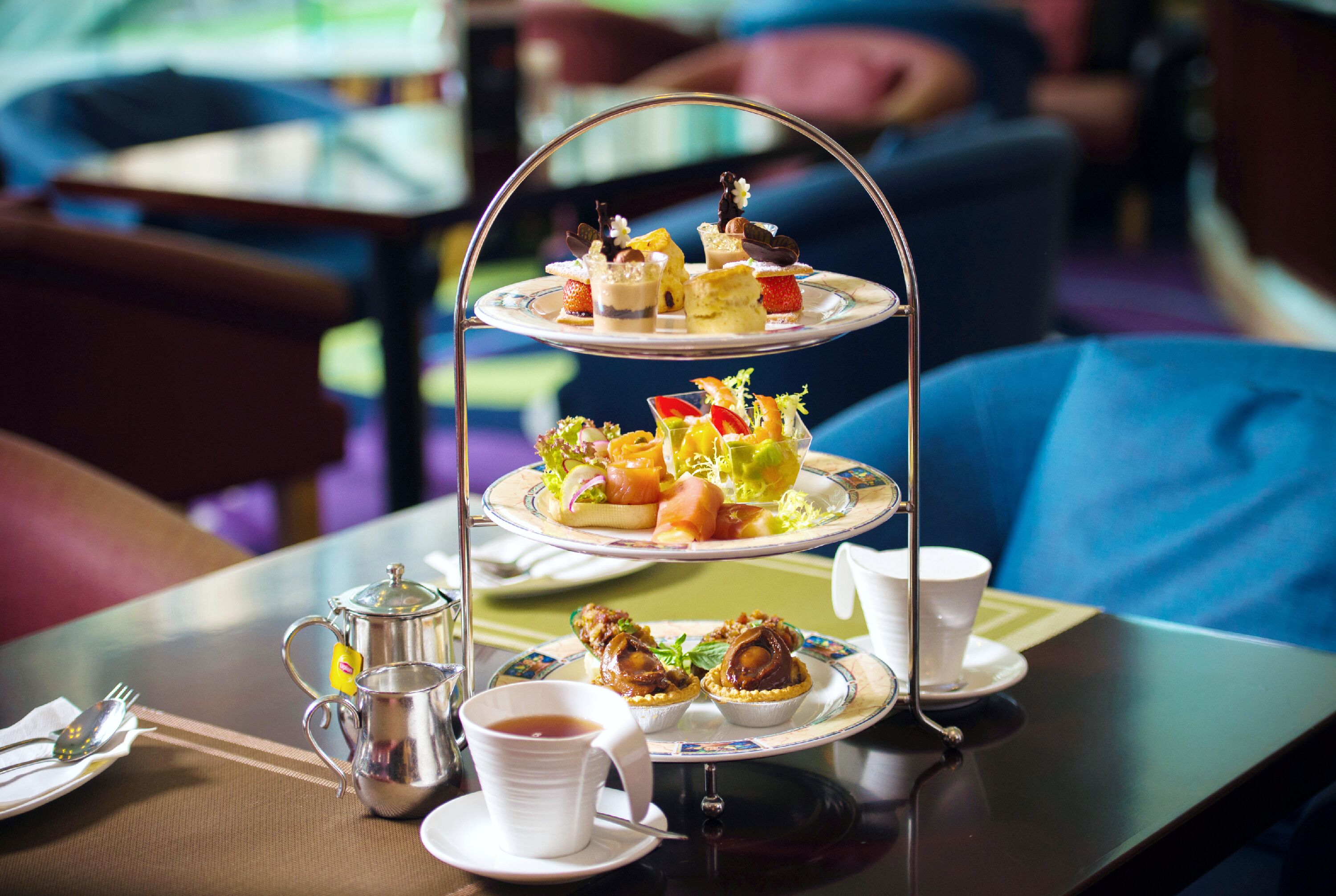 A three-tiered dessert stand with various pastries and a teapot on a table.