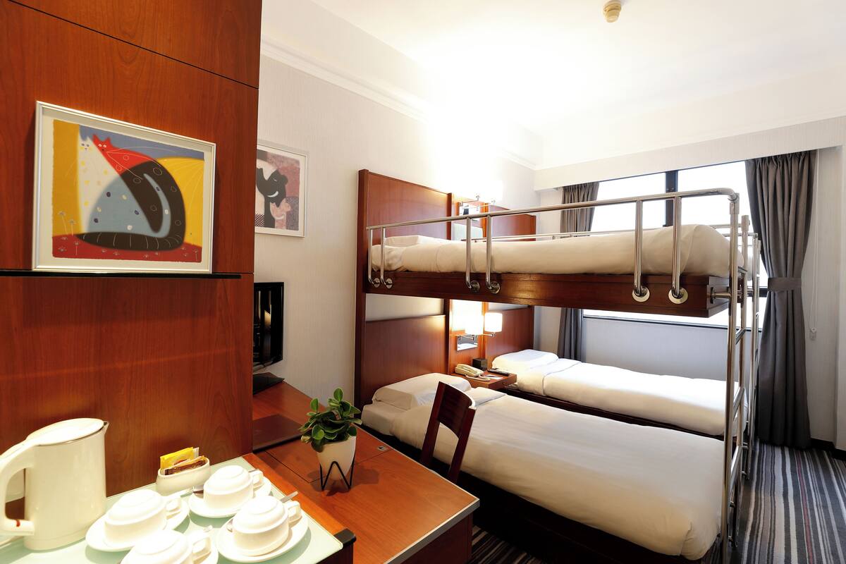 Una habitación de hotel con literas, una mesa de comedor con vajillas de té y un cuadro en la pared.