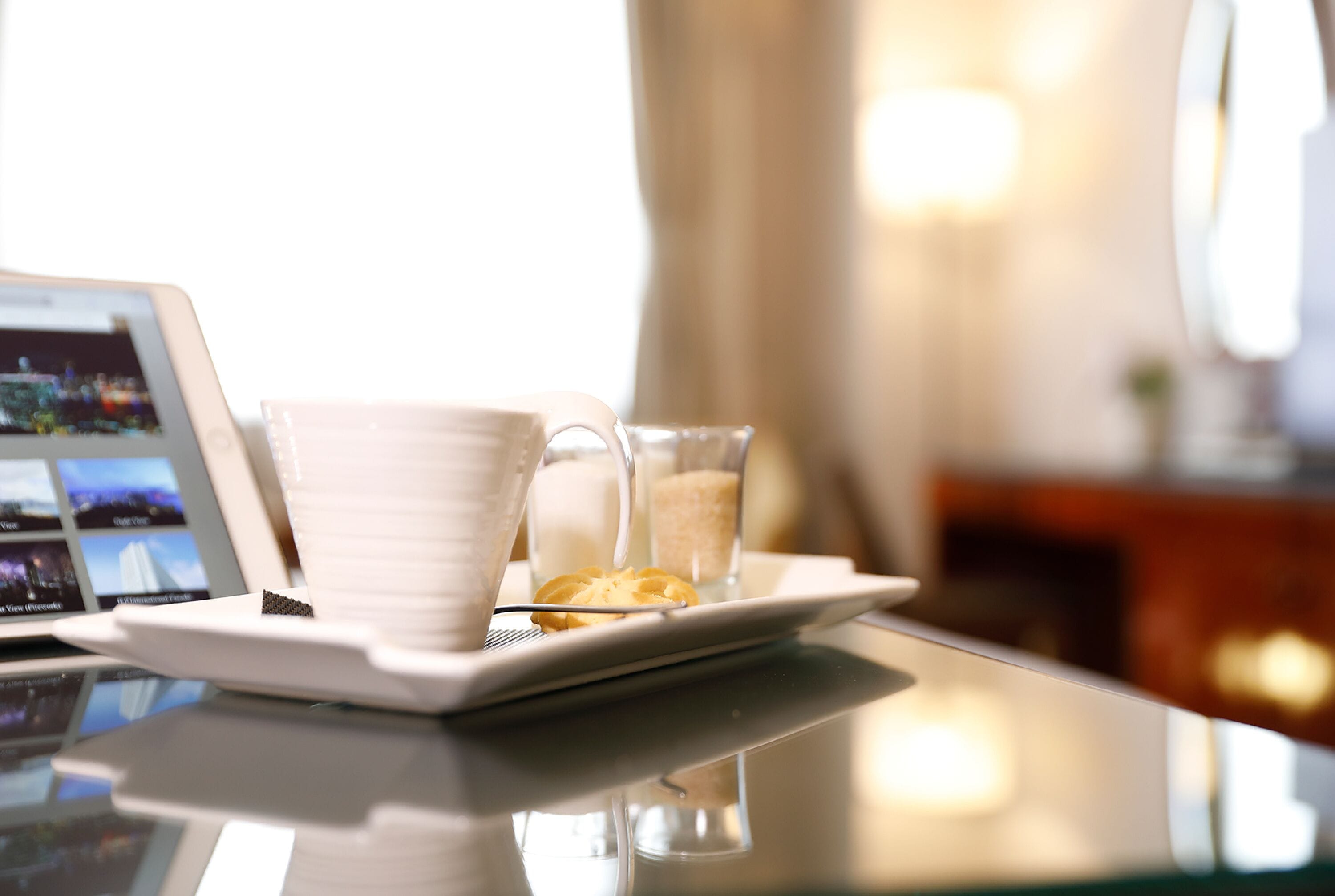 Una mesa con una computadora portátil, una taza blanca, un vaso de leche y un plato con una rodaja de limón.