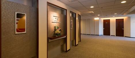 A hallway with a reception desk, numbered room signs, and a carpeted floor.
