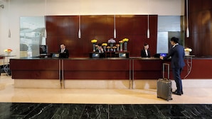 A hotel reception area with a marble floor, a reception desk, and a man with a suitcase. - B P International (Kowloon)