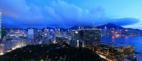 A cityscape at dusk with illuminated buildings and a body of water in the foreground.