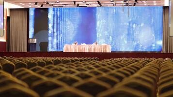 An auditorium with rows of seats, a stage with a large screen, and a podium.
