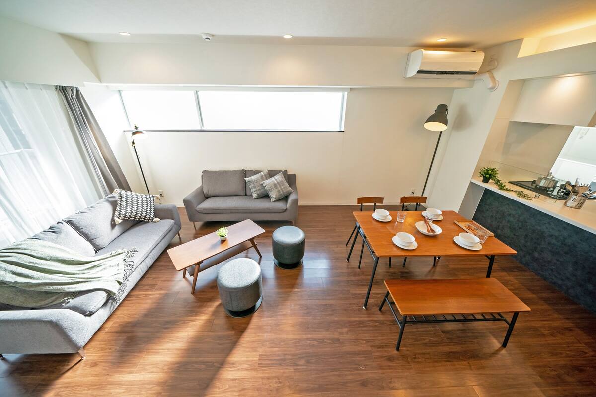 A modern living room with a sofa, ottomans, a dining table set for four, and a kitchen area with a sink and countertop.